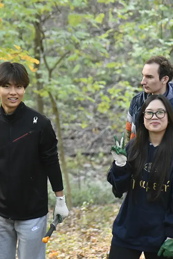 Students wearing work gloves smiling together outdoors during an environmental cleanup or volunteer project.